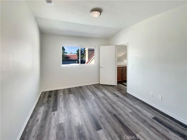 unfurnished room featuring dark wood-style flooring, baseboards, and vaulted ceiling