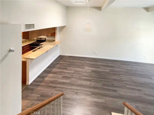 interior space with visible vents, a peninsula, brown cabinets, stainless steel gas range oven, and dark wood-style floors