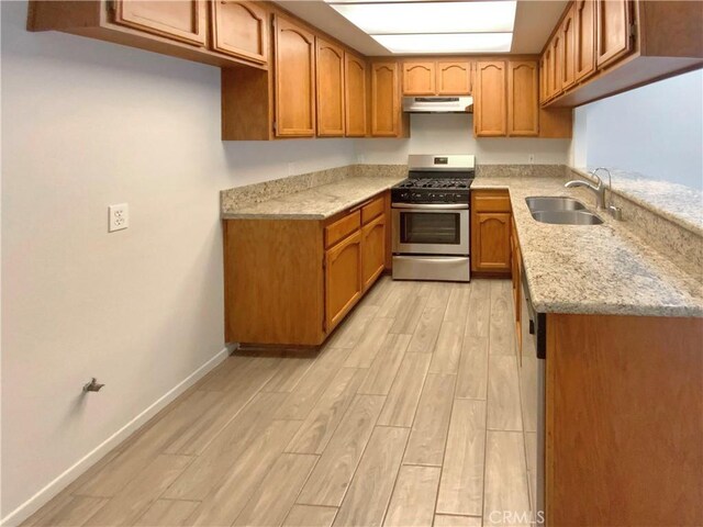 kitchen with stainless steel gas stove, a sink, brown cabinetry, under cabinet range hood, and wood finish floors