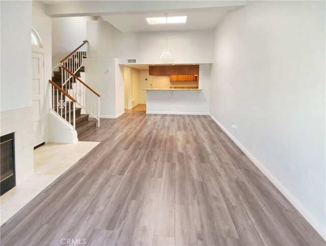 unfurnished living room featuring visible vents, light wood-style flooring, baseboards, stairs, and a fireplace