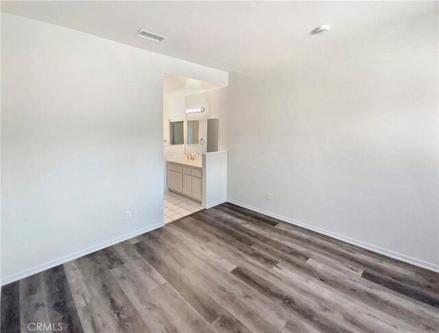 unfurnished bedroom with baseboards, visible vents, wood finished floors, and ensuite bath