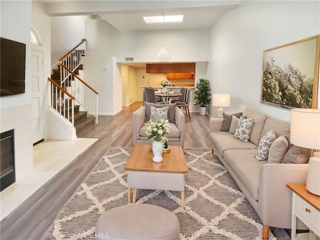 living room featuring high vaulted ceiling, a skylight, a tile fireplace, and light hardwood / wood-style flooring