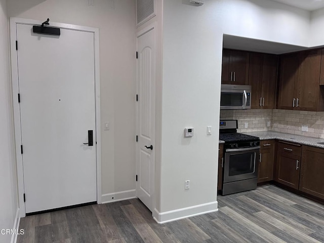 kitchen with light hardwood / wood-style flooring, appliances with stainless steel finishes, dark brown cabinets, tasteful backsplash, and light stone countertops