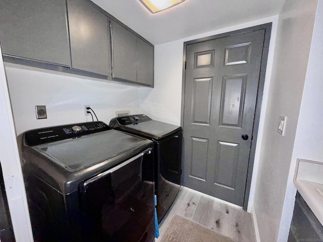 laundry area featuring washing machine and clothes dryer, light hardwood / wood-style flooring, and cabinets