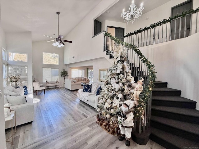 living room with ceiling fan with notable chandelier, light hardwood / wood-style floors, and high vaulted ceiling