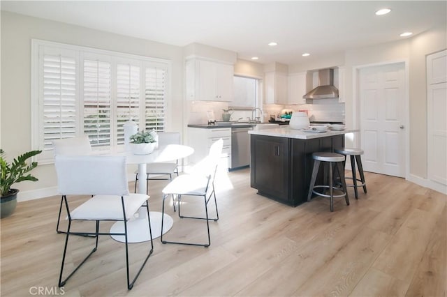 kitchen featuring wall chimney exhaust hood, dishwasher, a kitchen island, light hardwood / wood-style floors, and white cabinets