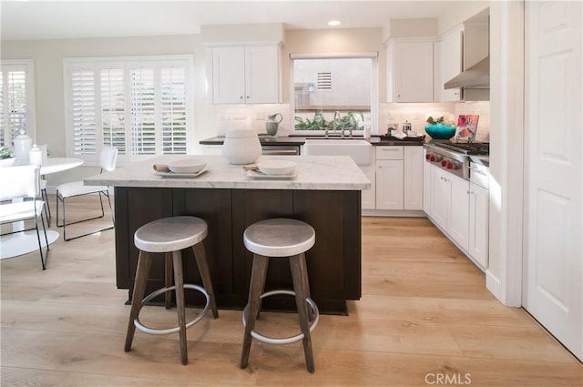 kitchen featuring extractor fan, stainless steel gas stovetop, white cabinetry, sink, and a center island