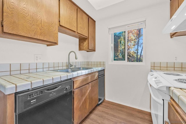 kitchen featuring ventilation hood, sink, black dishwasher, tile counters, and light hardwood / wood-style floors