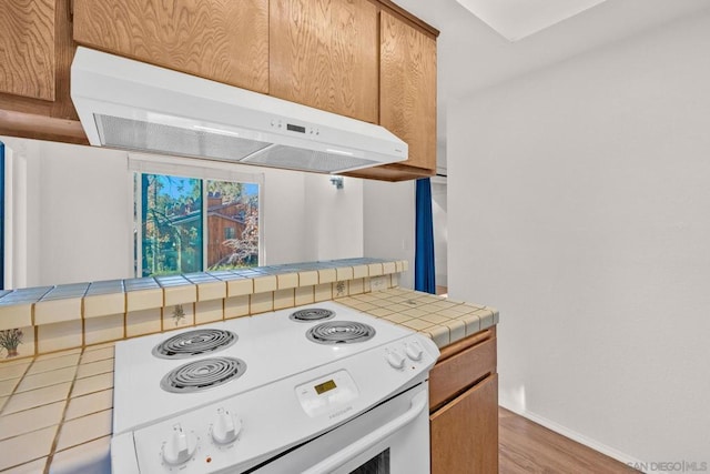 kitchen featuring wood-type flooring, ventilation hood, tile countertops, and electric stove