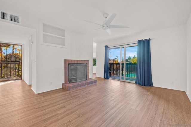 unfurnished living room with built in shelves, ceiling fan, a fireplace, and light hardwood / wood-style floors