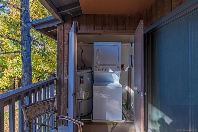 laundry room featuring wooden walls, water heater, and stacked washer and clothes dryer