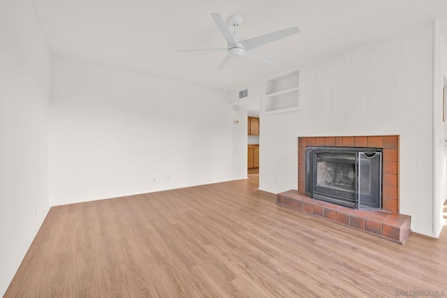 unfurnished living room with a tile fireplace, light wood-type flooring, built in features, and ceiling fan