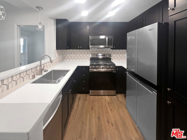 kitchen featuring sink, stainless steel appliances, tasteful backsplash, light hardwood / wood-style flooring, and decorative light fixtures