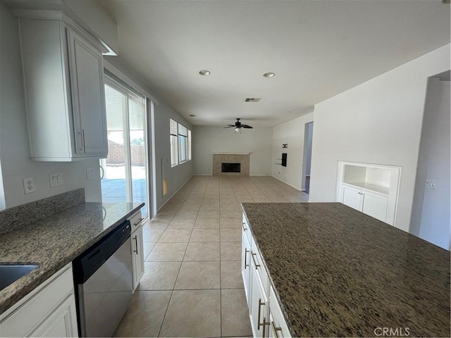 kitchen featuring white cabinets, a fireplace, ceiling fan, dark stone countertops, and dishwasher