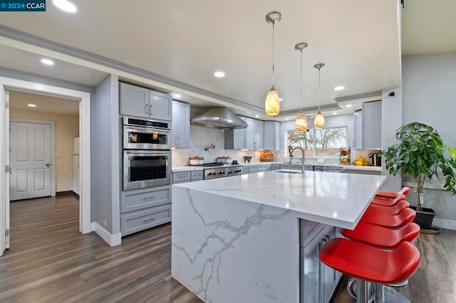 kitchen featuring appliances with stainless steel finishes, dark wood-type flooring, sink, wall chimney range hood, and a kitchen island