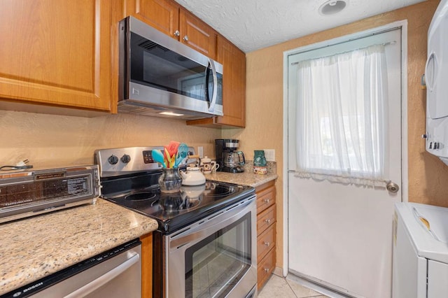 kitchen featuring light tile patterned flooring, appliances with stainless steel finishes, and light stone counters