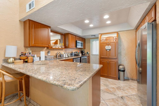 kitchen featuring a kitchen bar, stainless steel appliances, sink, kitchen peninsula, and light stone counters