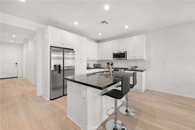 kitchen featuring white cabinetry, a center island with sink, light wood-type flooring, a kitchen breakfast bar, and stainless steel appliances