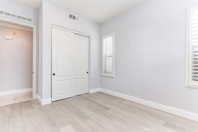 unfurnished bedroom with light wood-style flooring, a closet, visible vents, and baseboards