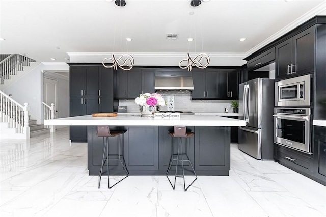 kitchen with appliances with stainless steel finishes, marble finish floor, light countertops, under cabinet range hood, and a kitchen bar