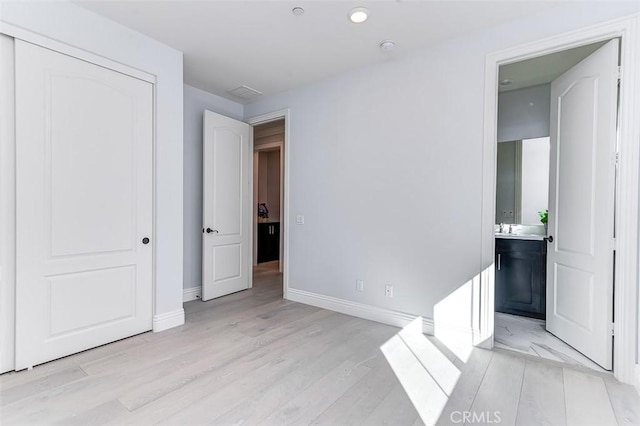 unfurnished bedroom featuring light wood-type flooring, a sink, ensuite bath, and baseboards