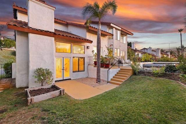 back house at dusk with french doors and a lawn