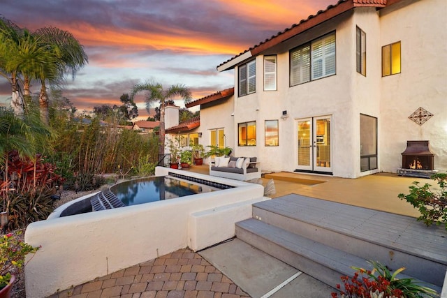 pool at dusk with an outdoor living space with a fireplace, a patio area, and french doors