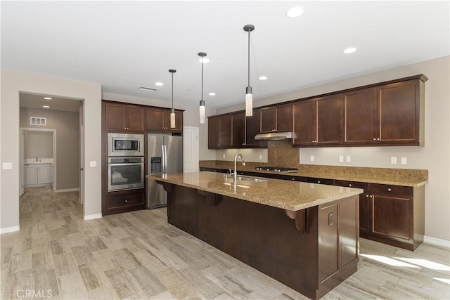 kitchen with a breakfast bar, sink, pendant lighting, stainless steel appliances, and light stone countertops