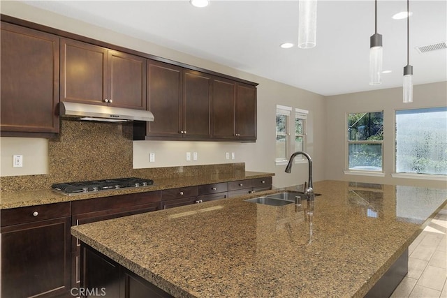 kitchen with stainless steel gas cooktop, dark brown cabinetry, sink, stone countertops, and pendant lighting