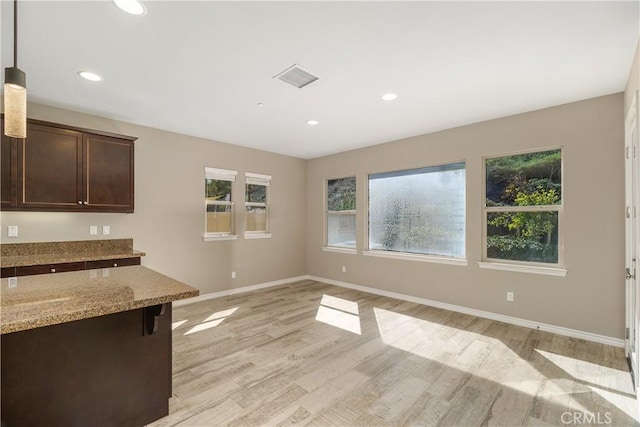 kitchen featuring light wood-type flooring, light stone countertops, decorative light fixtures, a healthy amount of sunlight, and dark brown cabinetry