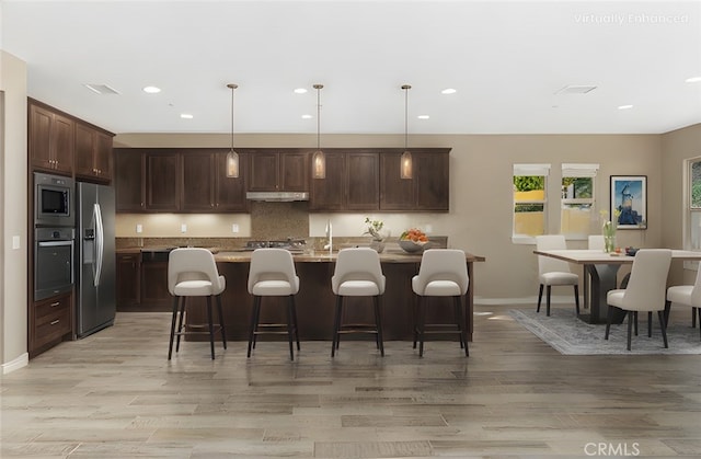 kitchen with a center island with sink, a kitchen bar, stainless steel appliances, and decorative light fixtures