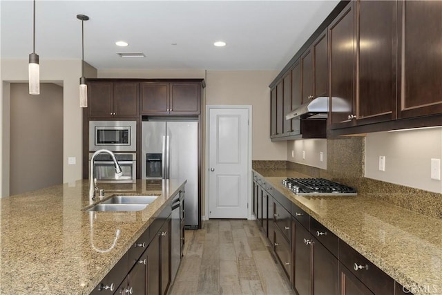 kitchen with appliances with stainless steel finishes, sink, light stone counters, hanging light fixtures, and dark brown cabinets