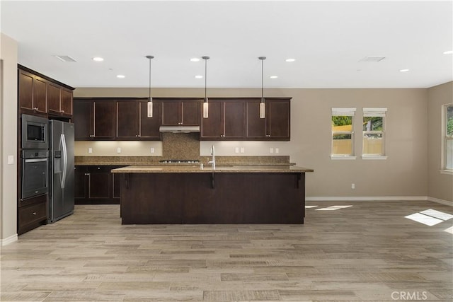 kitchen featuring an island with sink, appliances with stainless steel finishes, stone counters, and decorative light fixtures
