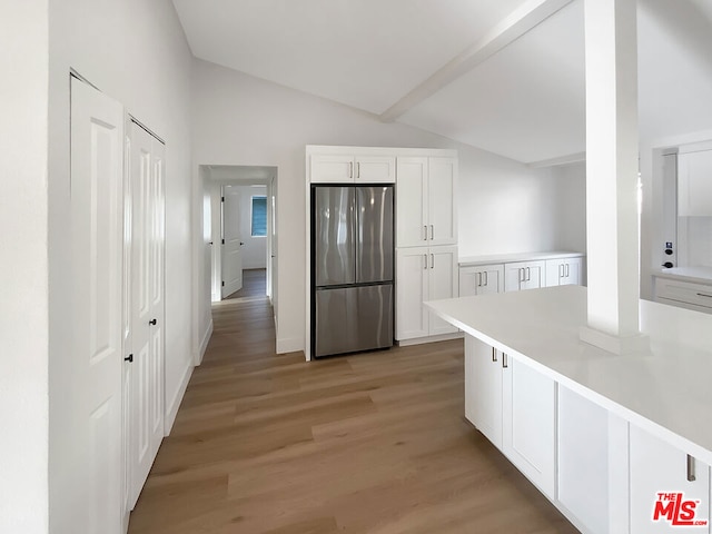 kitchen with white cabinets, vaulted ceiling with beams, light hardwood / wood-style flooring, and stainless steel refrigerator