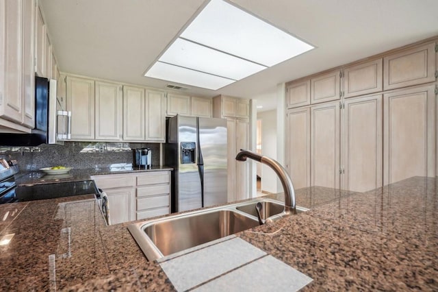 kitchen with appliances with stainless steel finishes, sink, dark stone counters, decorative backsplash, and cream cabinetry