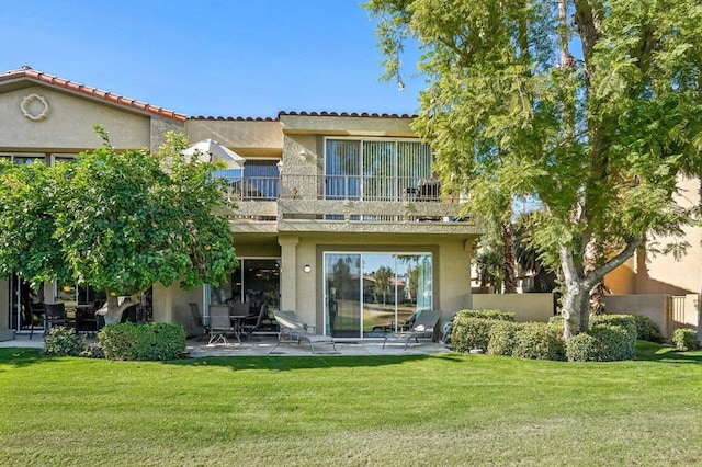 rear view of house featuring a patio, a balcony, and a lawn