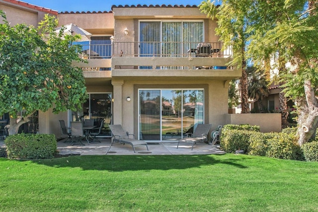 back of property featuring a balcony, a patio area, and a lawn