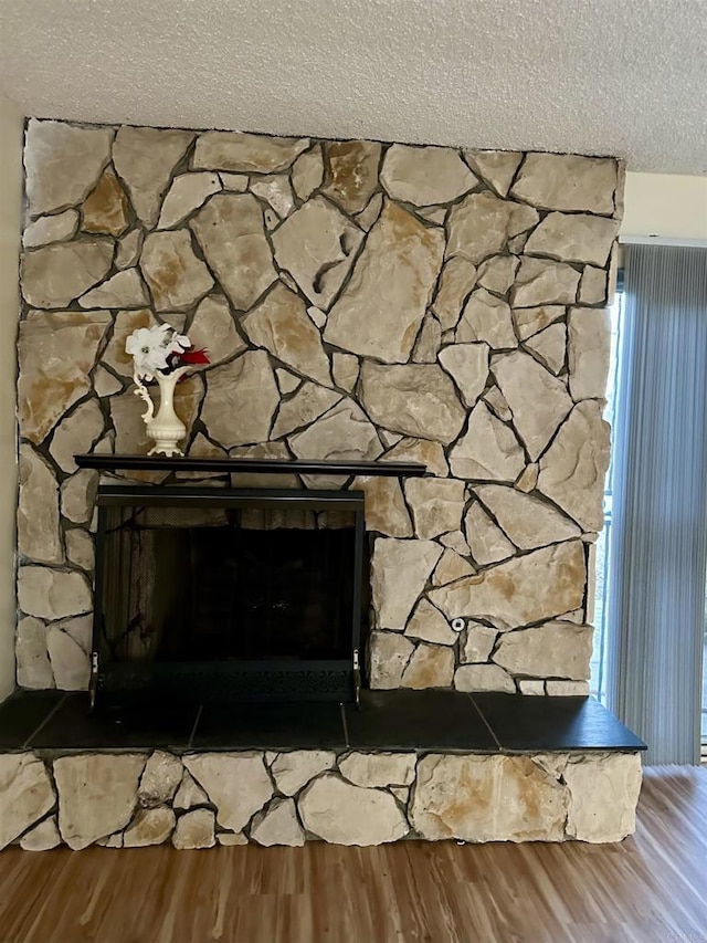 interior details with wood-type flooring, a textured ceiling, and a stone fireplace