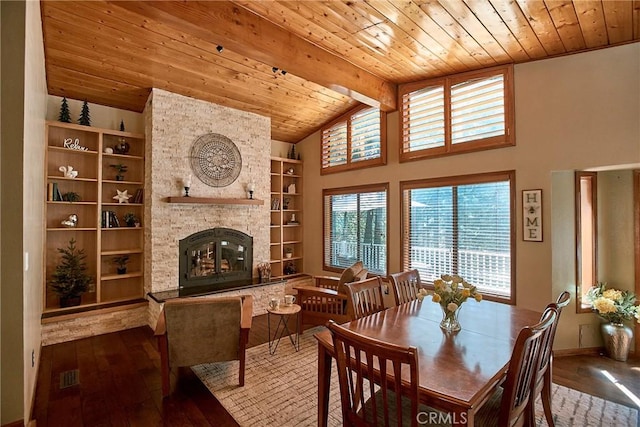 dining space with built in shelves, beam ceiling, a stone fireplace, wooden ceiling, and hardwood / wood-style flooring