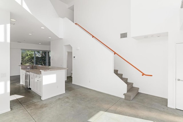 kitchen with a high ceiling, white cabinets, dishwasher, a kitchen island, and sink