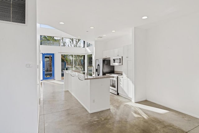 kitchen featuring white cabinets, a towering ceiling, stainless steel appliances, an island with sink, and a breakfast bar area