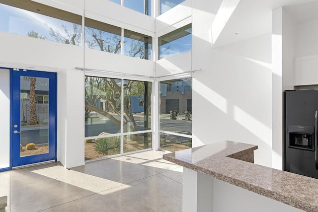 interior space with black fridge, a towering ceiling, and concrete flooring