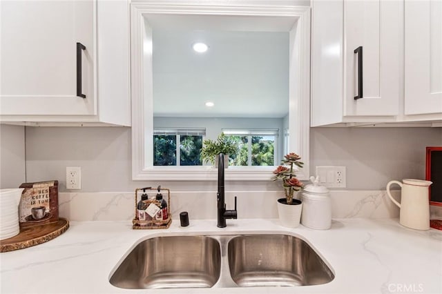 room details featuring light stone counters, white cabinetry, and sink