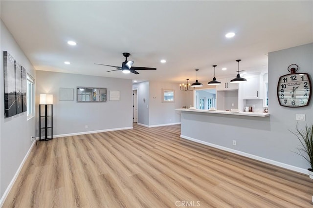 unfurnished living room featuring ceiling fan with notable chandelier and light wood-type flooring