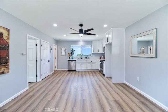 kitchen with appliances with stainless steel finishes, light wood-type flooring, ceiling fan, sink, and white cabinetry