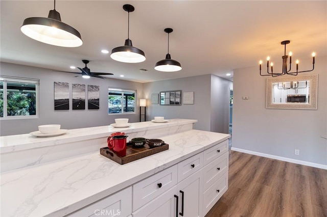 kitchen with light stone countertops, ceiling fan with notable chandelier, pendant lighting, hardwood / wood-style floors, and white cabinetry