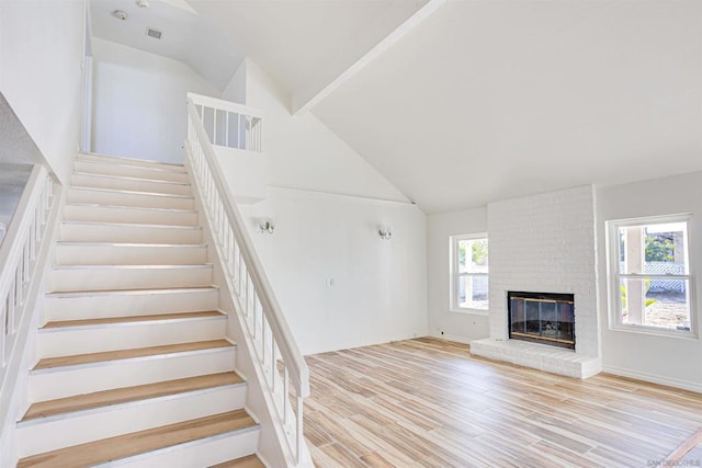 stairs with plenty of natural light, a brick fireplace, high vaulted ceiling, and wood-type flooring