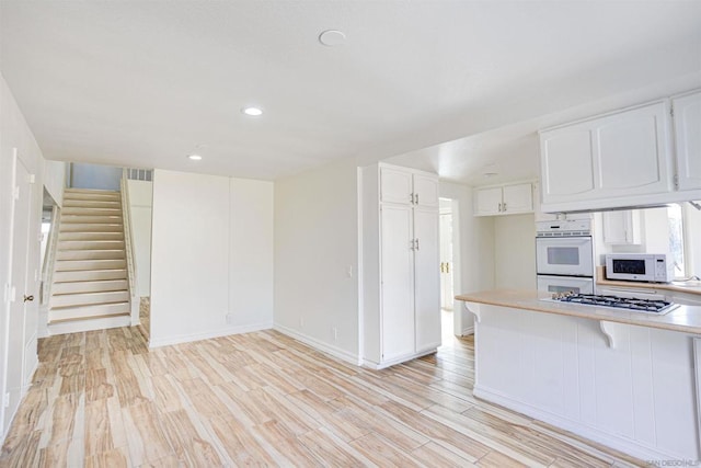 kitchen featuring a kitchen bar, light hardwood / wood-style flooring, kitchen peninsula, white appliances, and white cabinets