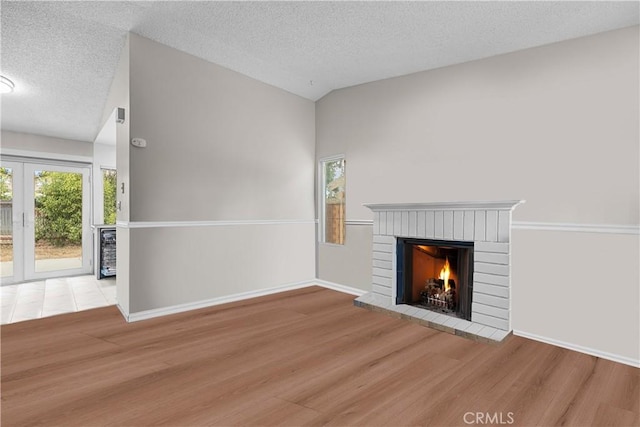 unfurnished living room featuring light wood-type flooring, vaulted ceiling, a brick fireplace, and a textured ceiling