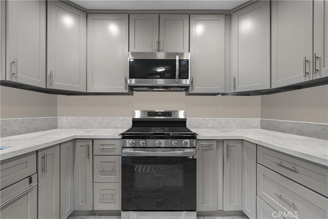 kitchen with light stone counters, gray cabinets, and stainless steel appliances